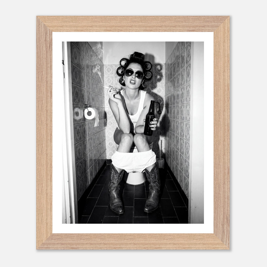 Black and white photograph of a rebellious cowgirl wearing cowboy boots and sunglasses sitting in a tiled restroom holding a cigarette and beer.