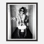 Black and white photograph of a rebellious cowgirl wearing cowboy boots and sunglasses sitting in a tiled restroom holding a cigarette and beer.