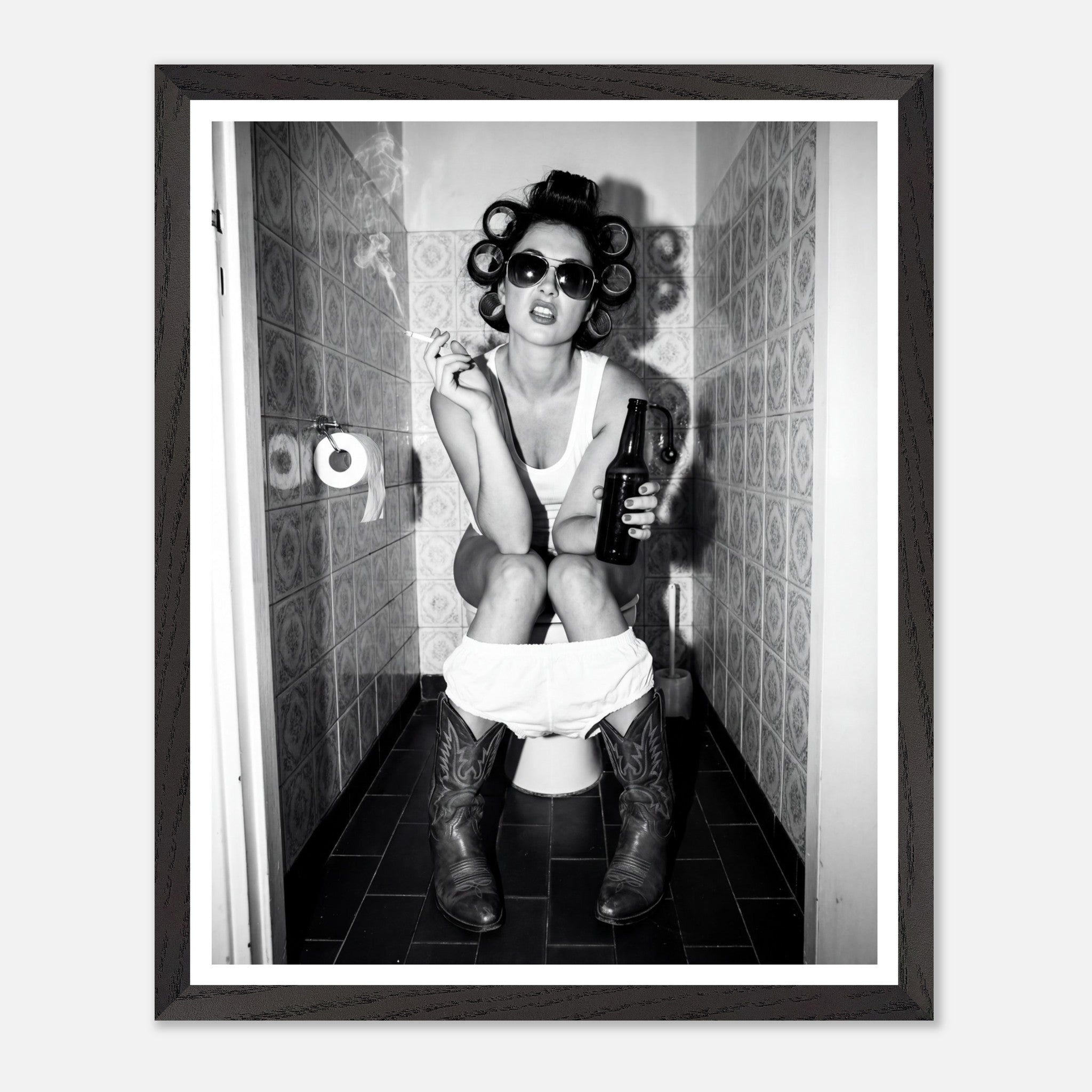 Black and white photograph of a rebellious cowgirl wearing cowboy boots and sunglasses sitting in a tiled restroom holding a cigarette and beer.