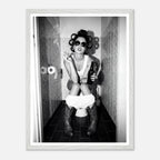 Black and white photograph of a rebellious cowgirl wearing cowboy boots and sunglasses sitting in a tiled restroom holding a cigarette and beer.