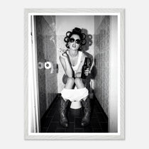 Black and white photograph of a rebellious cowgirl wearing cowboy boots and sunglasses sitting in a tiled restroom holding a cigarette and beer.