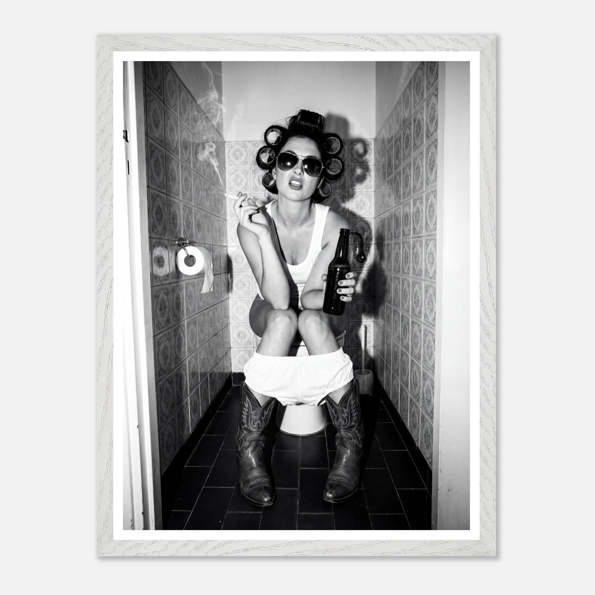 Black and white photograph of a rebellious cowgirl wearing cowboy boots and sunglasses sitting in a tiled restroom holding a cigarette and beer.