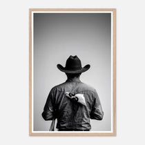 Black and white photograph of a rodeo cowboy viewed from behind wearing a western hat with a numbered rodeo tag pinned to his shirt after competition.