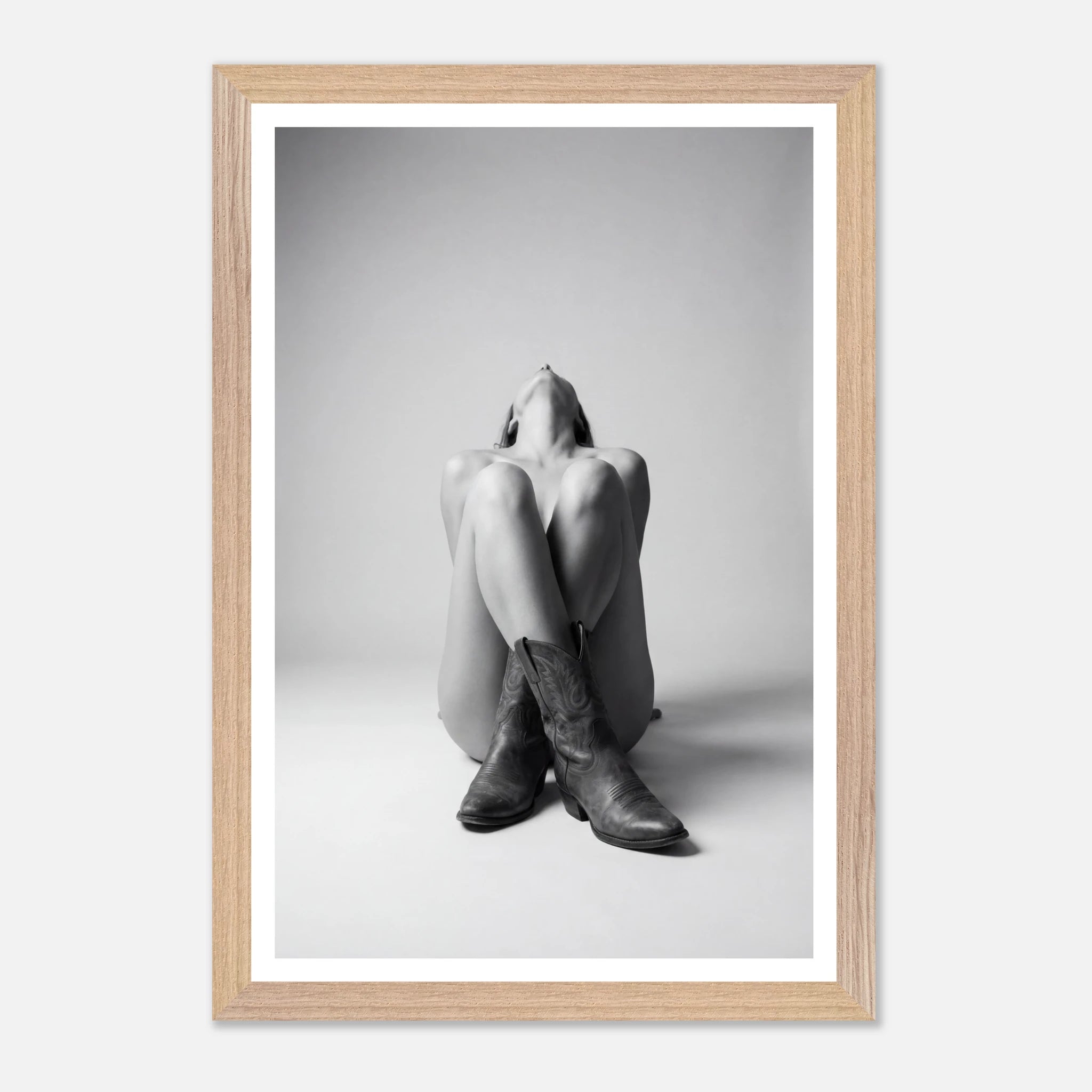 Framed black and white photo of a person sitting with legs crossed wearing cowboy boots.