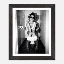 Black and white photograph of a rebellious cowgirl wearing cowboy boots and sunglasses sitting in a tiled restroom holding a cigarette and beer.
