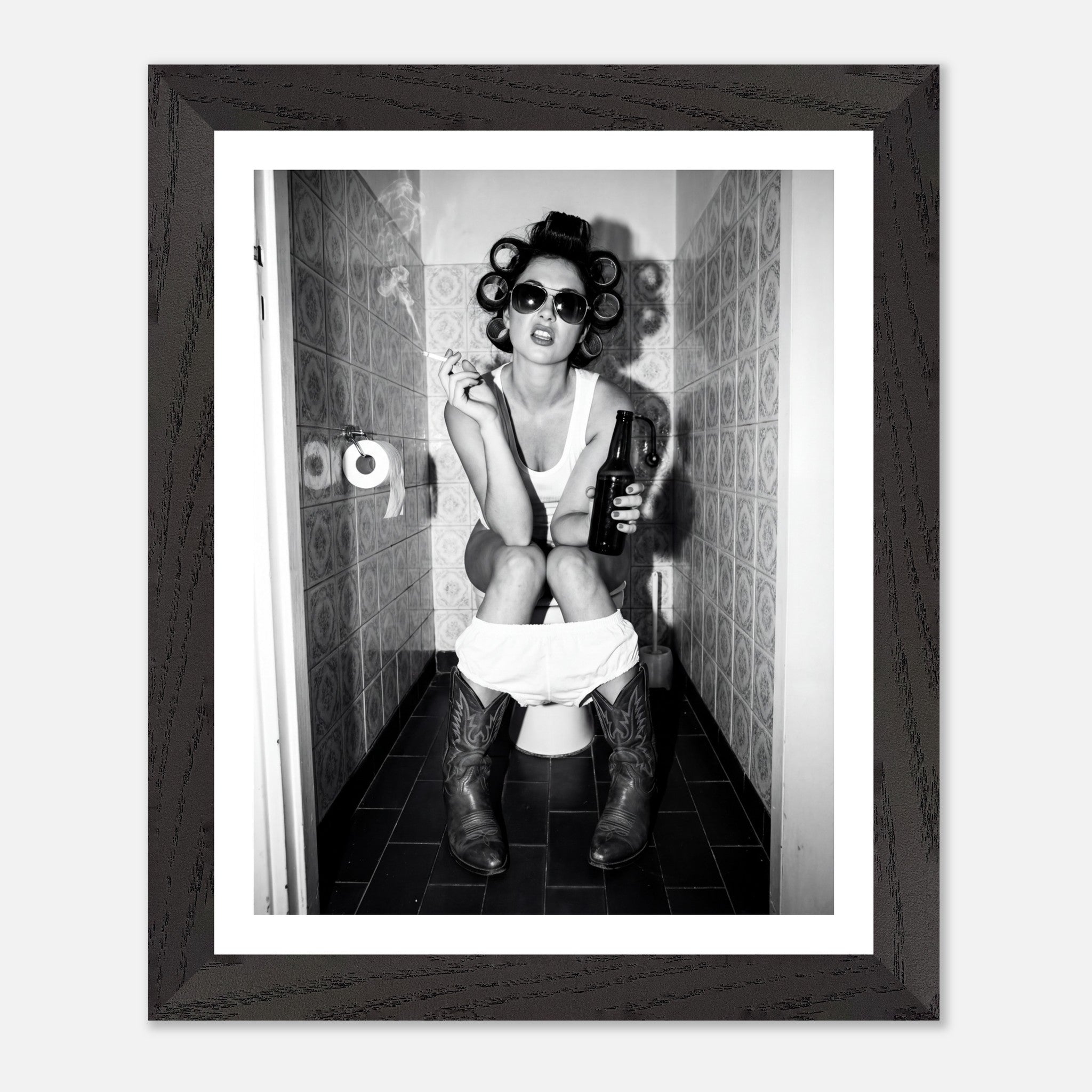 Black and white photograph of a rebellious cowgirl wearing cowboy boots and sunglasses sitting in a tiled restroom holding a cigarette and beer.
