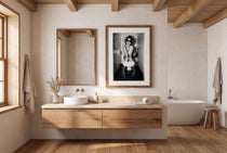 Black and white photograph of a rebellious cowgirl wearing cowboy boots and sunglasses sitting in a tiled restroom holding a cigarette and beer.