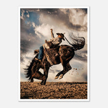 Cowboy riding a bucking horse at sunset with dust and dramatic sky, western rodeo wall art print