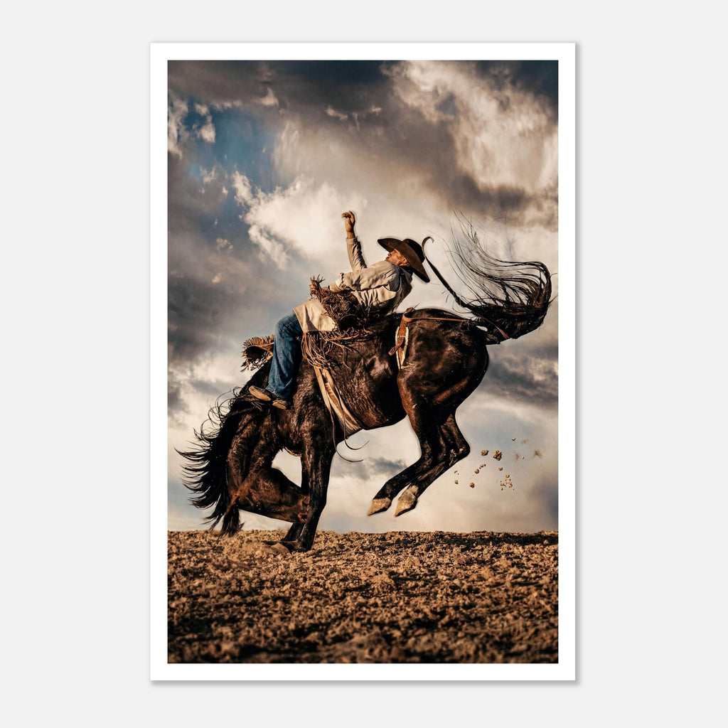 Cowboy riding a bucking horse at sunset with dust and dramatic sky, western rodeo wall art print